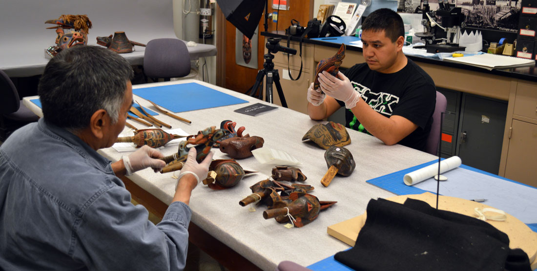 two men examine objects on a table in the Burke collection area