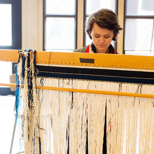 a woman weaves a chilkat blanket on a large loom