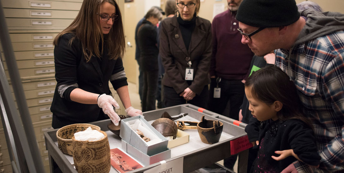 a young woman holds an object to show visitors to the collection