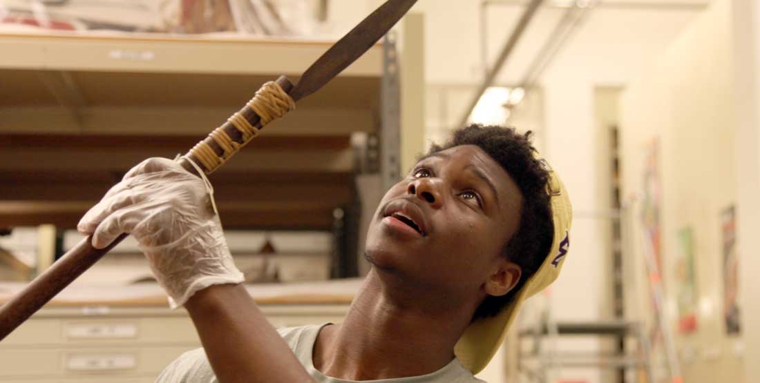 A young man examines a spear in the museum collections