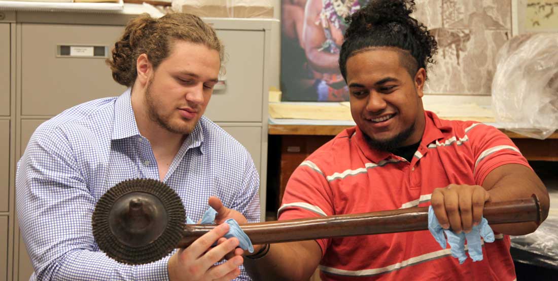 Two young men examine a large club in the museum collections