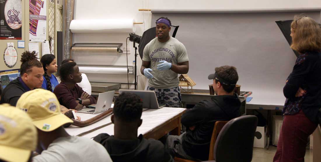 A college-aged student presents his research in front of his classmates while in the Burke Museum collections space