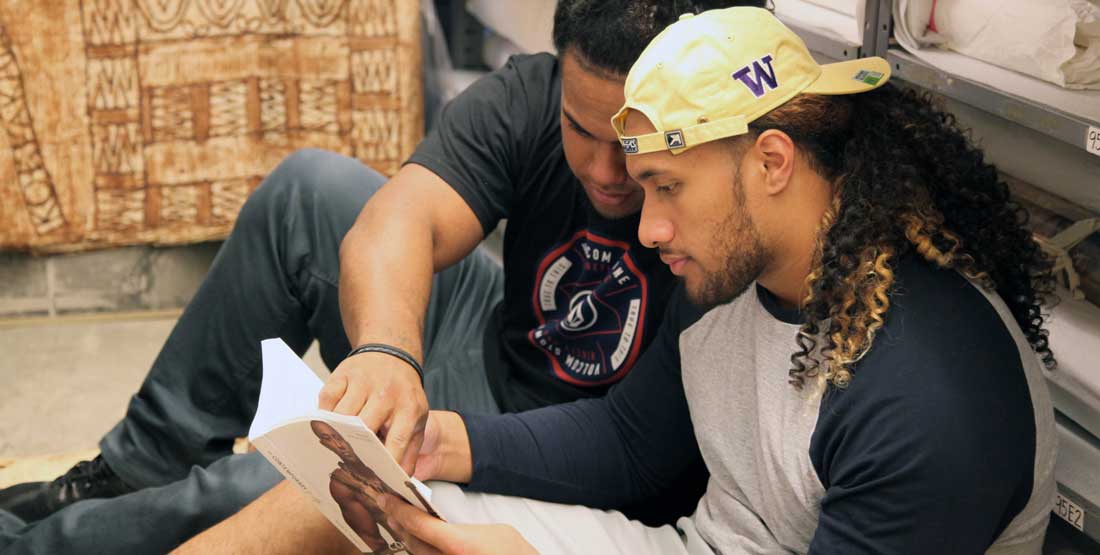 Two young men look point to an object in a book