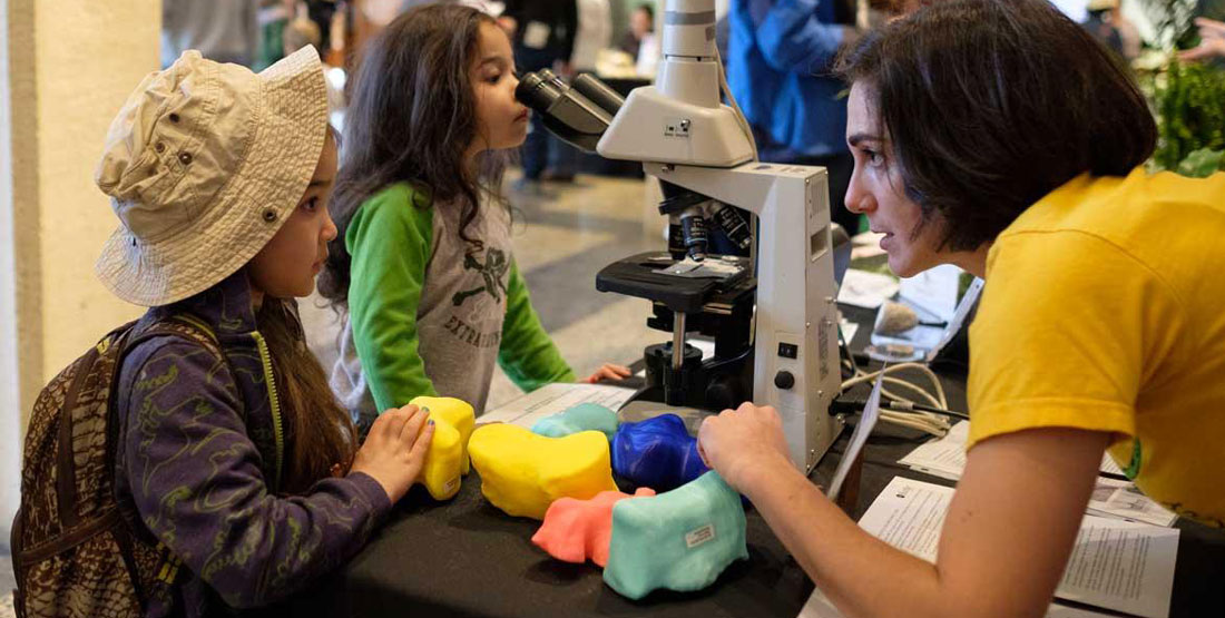 two girls talk to a volunteer at a busy event