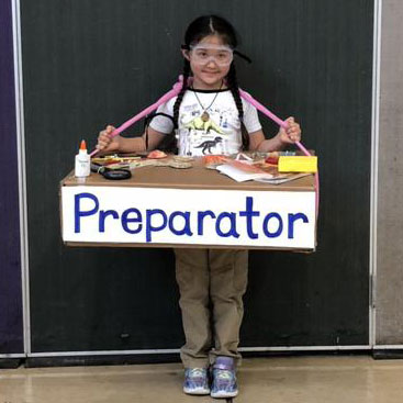 a girl stands wearing a handmade cardboard fossil prep table on her front