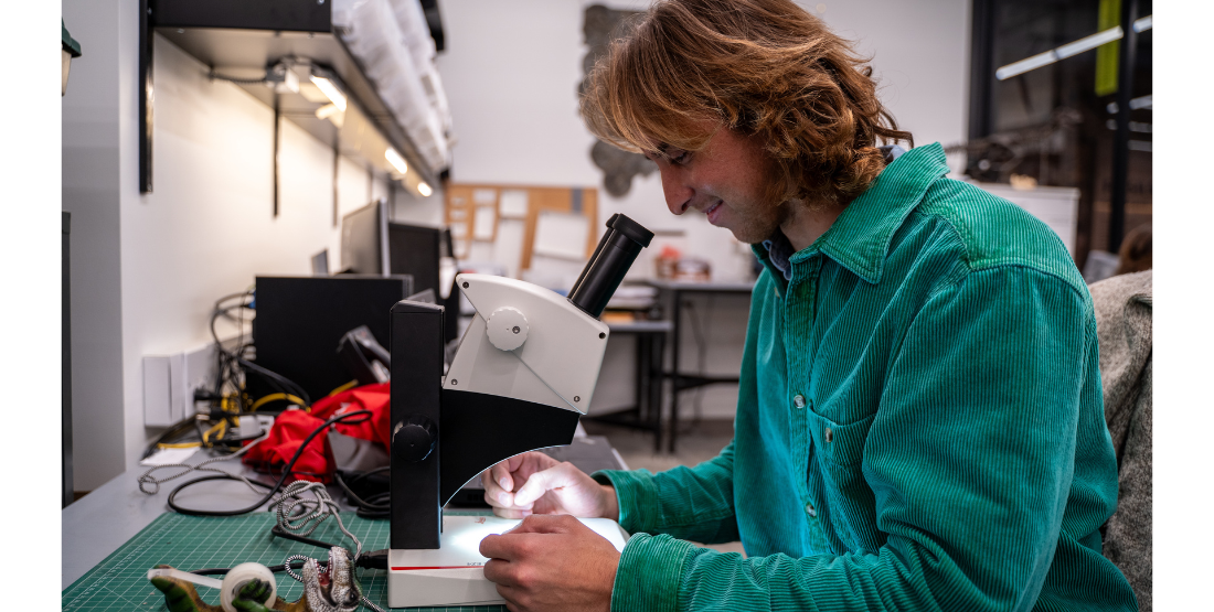 Man in green shirt looks through a microscope in a science lab.