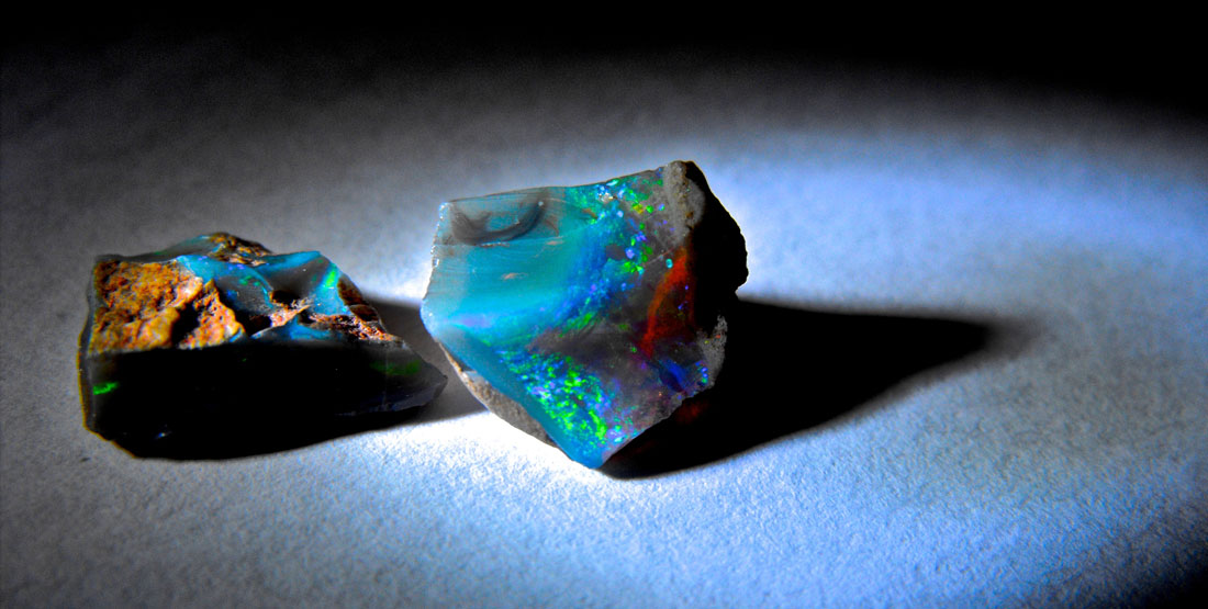 Two multi-colored rough opals sit on a table
