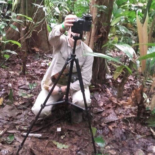 a young woman kneels while taking a photo with a camera pointed straight up on a tripod