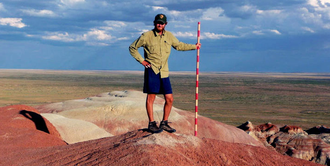 A male researcher stands in the Wyoming desert holding a red and white striped pole