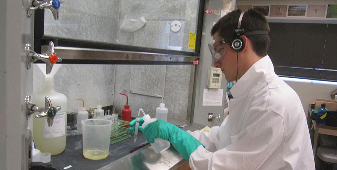 a young man wears a white lab coat and gloves while extracting phytolith samples in a lab