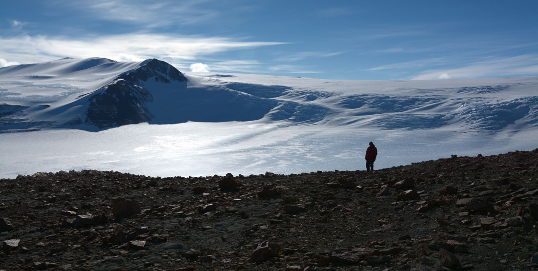 scenic shot of a person standing on an antarctica rock outcrop showing ice in the background
