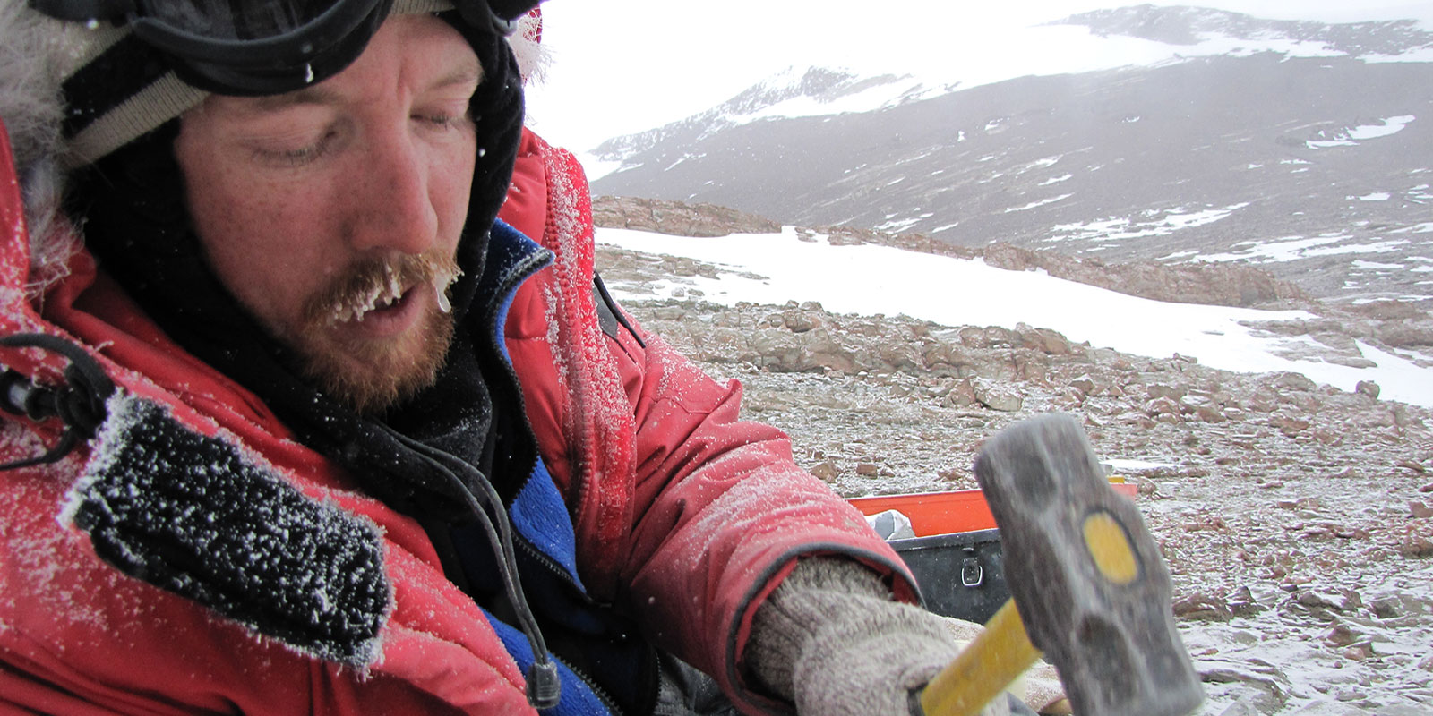 A man with frosh on his jacket and bear uses a mallot on the landscape
