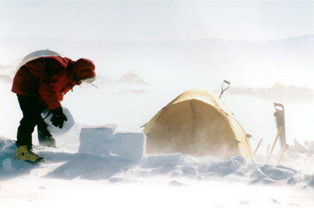 A man bundled in snow gear stacks blocks of snow on top of each other