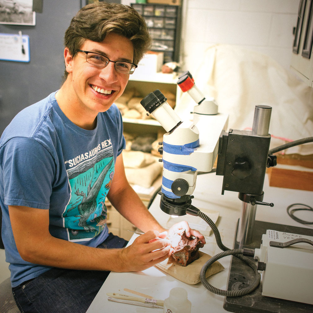 a young man uses a miniature jackhammer to remove rock from washington's first dinosaur fossil