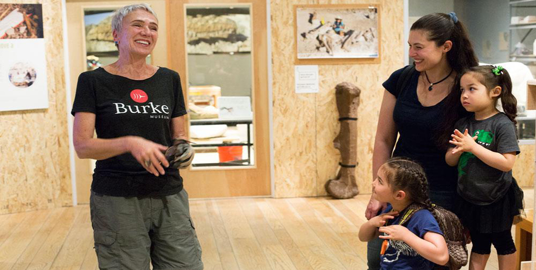 A mom and her two young daughters stand with a Burke t. rex preparator volunteer