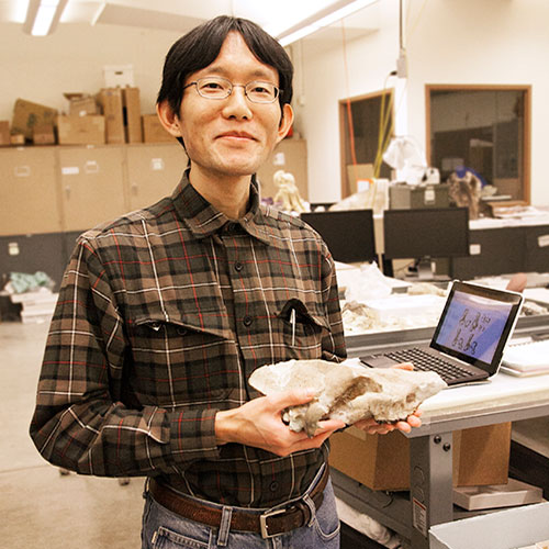 A male researcher holds a fossil with a computer in the background