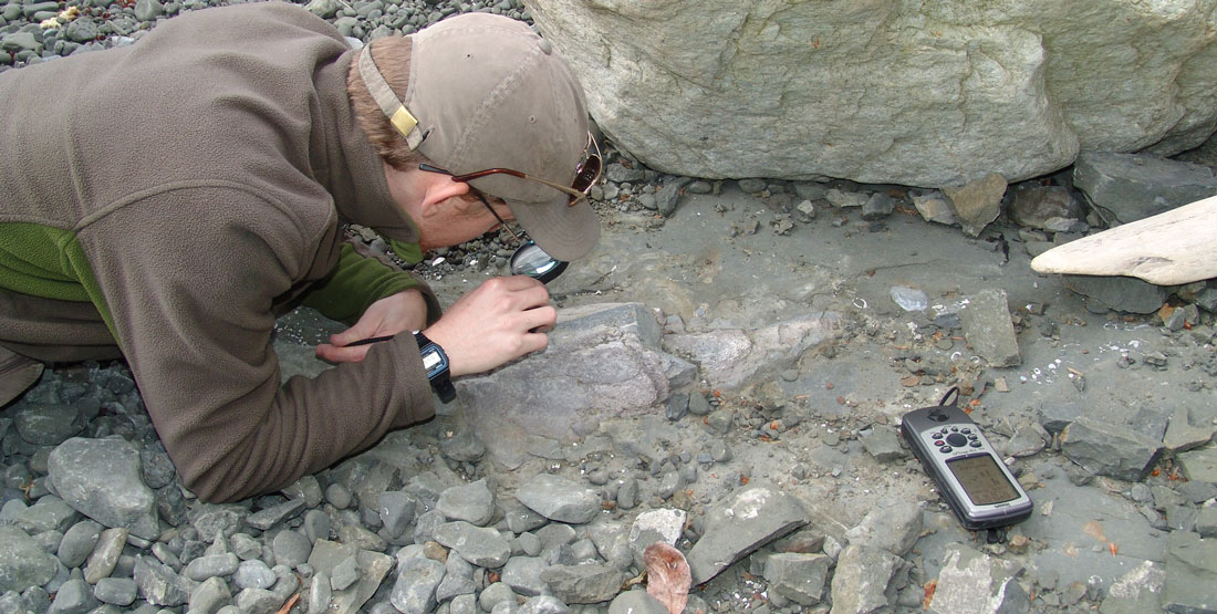 a man lays on the ground and closely examines the exposed bone with a magnifying glass