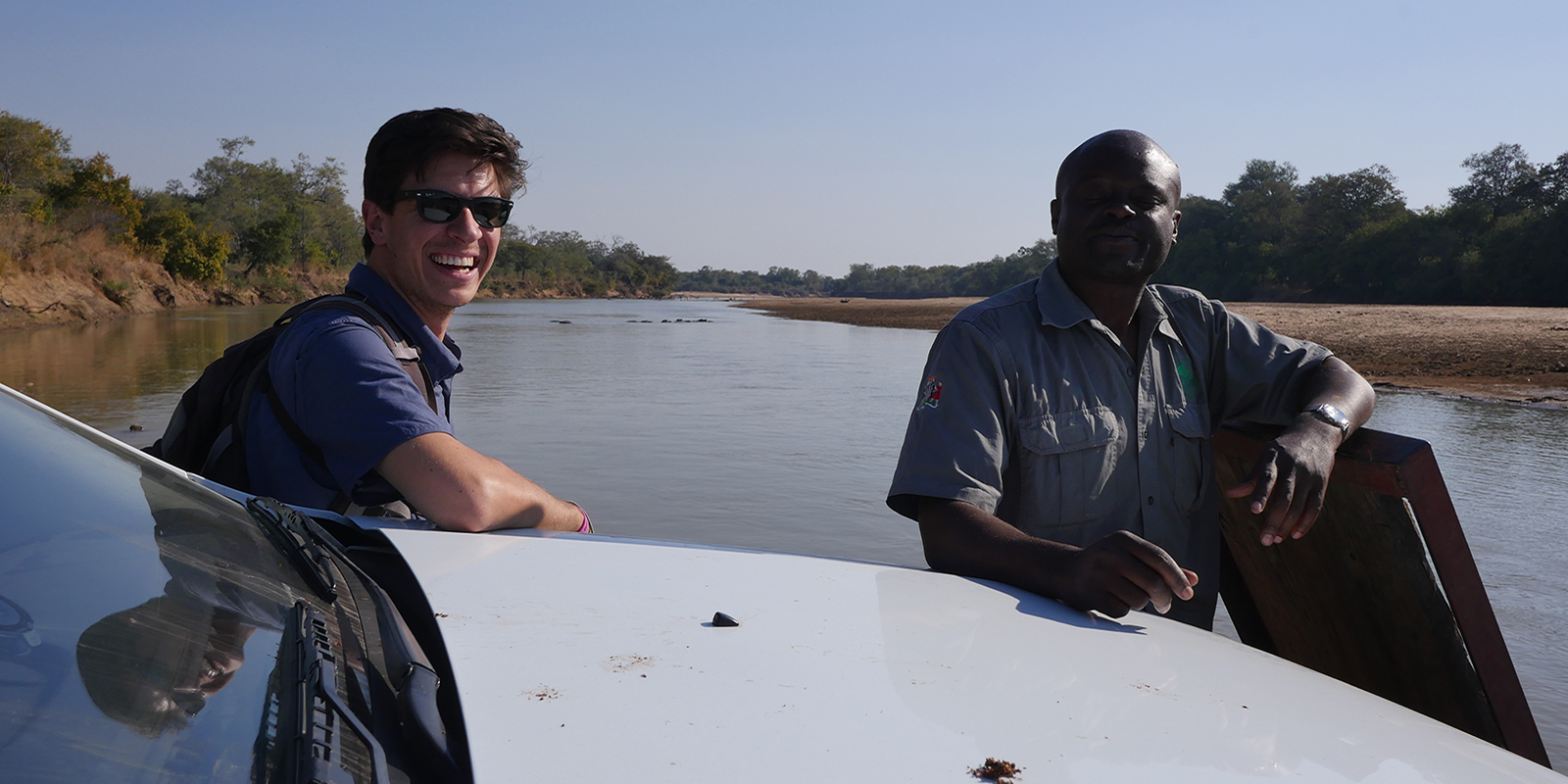 Two men smile with the river in the background