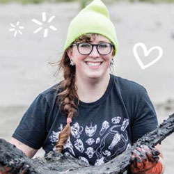 a young woman stands holding a whale vertebrae while cleaning it on the beach