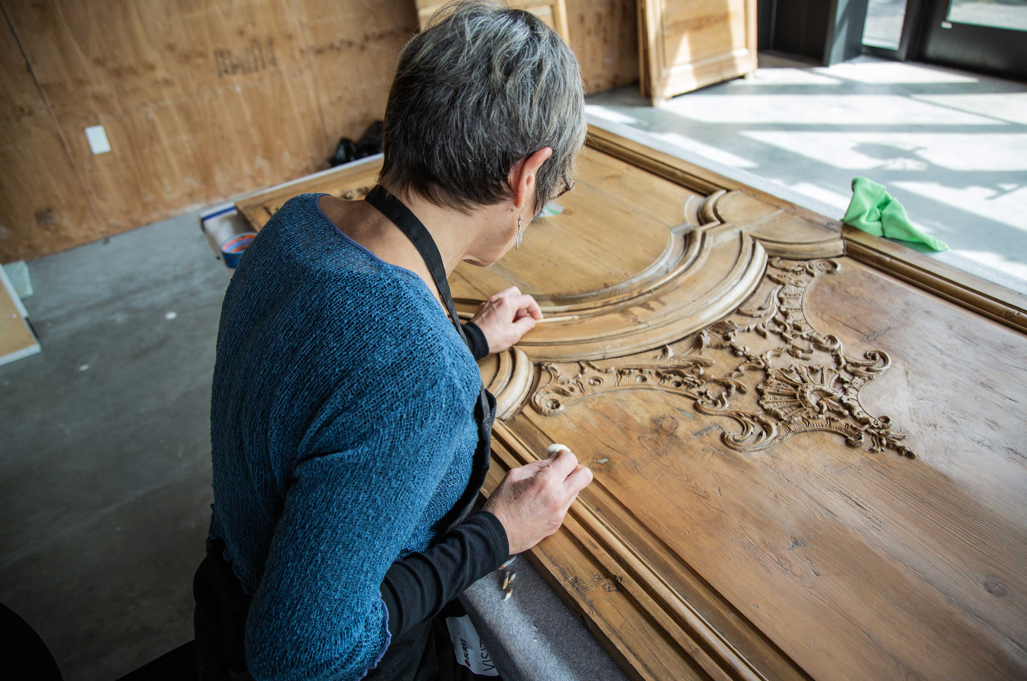 A woman gently cleans the boiserie panel with a cotton ball