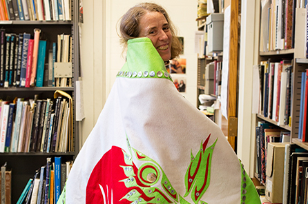 A woman wears a green, red, and white button blanket with Burke logo and eagle design