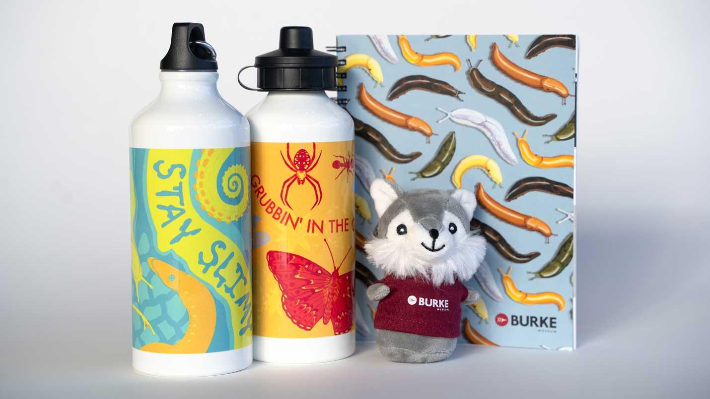 two water bottles, a sketchbook with a slug design on it, and a small plush husky dog toy wearing a Burke shirt