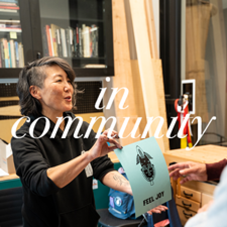 an artist holds up a paper with a relief print that says FEEL JOY