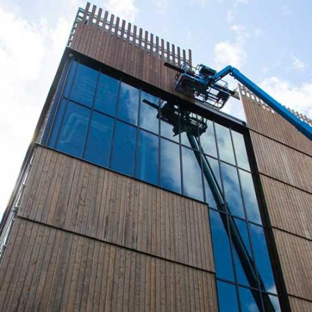 A crew member uses a lift to install siding with the lift reflecting in the glass