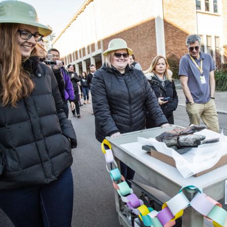 a team rolls a cart with a dinosaur fossil past the burke staff and volunteers cheering them on