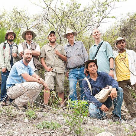 A group of 8 professors and students pose for a photo in the field 