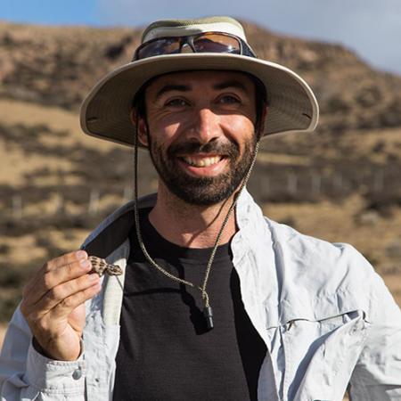 a young man holds a small lizard while researching in the field