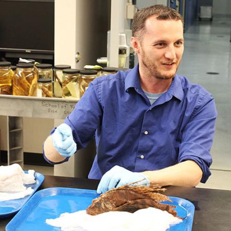 a man wears gloves and holds a preserved fish specimen