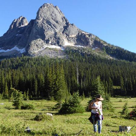 a woman searches the ground in a forest with a mountain peak off in the distance