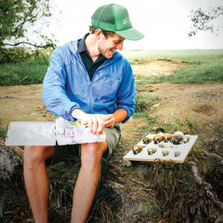 A male researcher in a green baseball cap prepares his tools for examining the birds he has collected