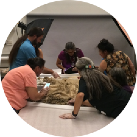 a group of men and women look closely at objects on a large table