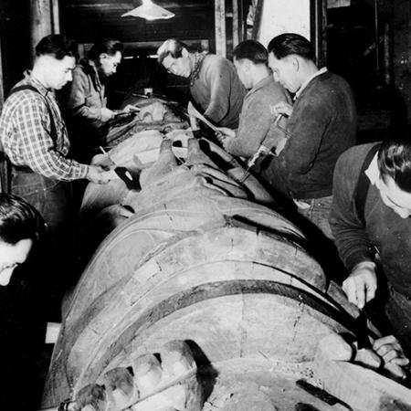 A black and white photo of men working on a totem pole