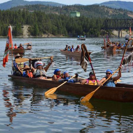 A group of people in traditional native clothes paddle a canoe