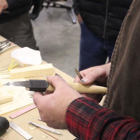 A hand holds a finished crooked knife with a wooden handle