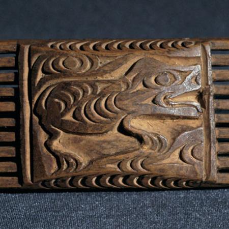 A comb with a four-legged animal is shown with a clear profile, its tail curled up over the head and negative crescents and trigons defining the ribs.