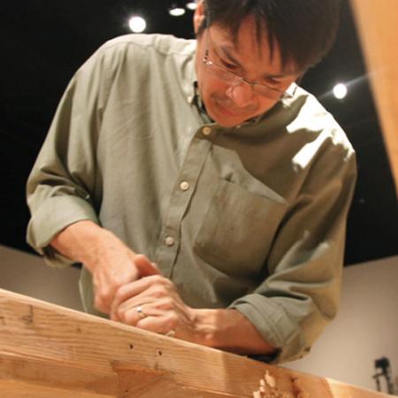 A researcher uses a hand tool to carve an Angyaaq boat