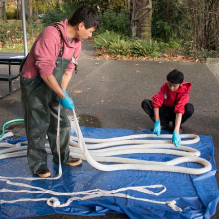 A researcher and a child stand on a blue tarp outside holding a long tubular-looking bear gut
