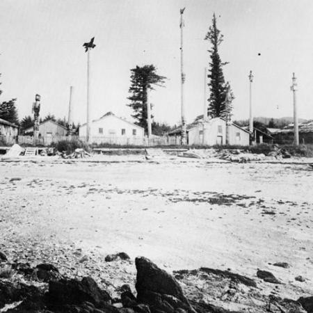 historic black and white photograph of First Nations village with numerous totem poles next to structures