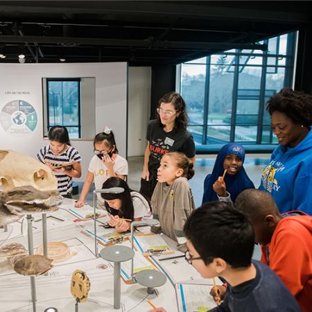 a group of students and teachers stand in front of an exhibit with skeletons and plants