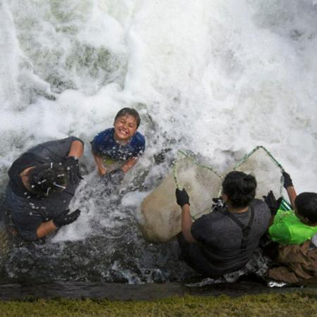 a young boy smiles while standing in a swift river with other youth