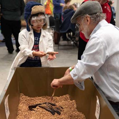 a kid and an adult dig in a dig pit to reveal a fossil cast