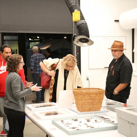 a burke researcher speaks with two visitors with a large basket and artifacts out on the table