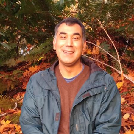 a man poses for a portrait with trees behind him