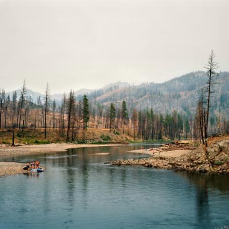 A group of people prepare to swim in a river; the surrounding landscape has been affected by wildfires