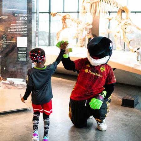 a child high fives sammy the sounder mascot at sounders fc day at the burke museum