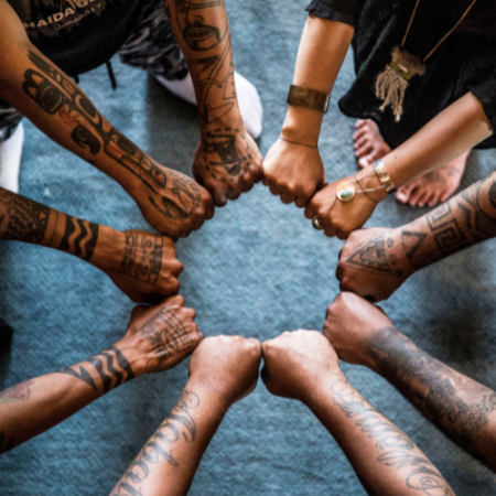people stand in a circle, stretching their arms into the center to form a circle with their fists